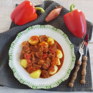 Goulash: een Hongaarse stoofschotel van rundvlees, paprika en uien. De goulash ligt in een bord met gekookte aardappels.
