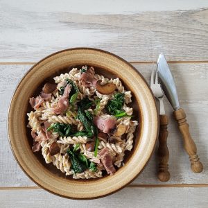 Een bord fusili met rauwe ham en champignons.