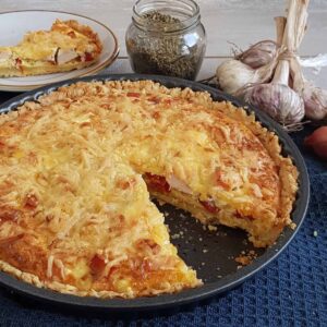 Quiche met gerookte kip en paprika in een quichevorm. Uit de quiche is een punt gesneden zodat de vulling zichtbaar is.