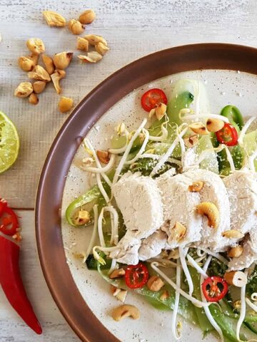 Gepocheerde kokoskip met komkommersalade op een bord, met limoen, rode peper en cashewnoten als garnering.