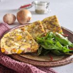 Zijaanzicht van een stuk frittata met aardappel, paprika en chorizo. De omelet is opengesneden zodat de ingrediënten goed zichtbaar zijn.