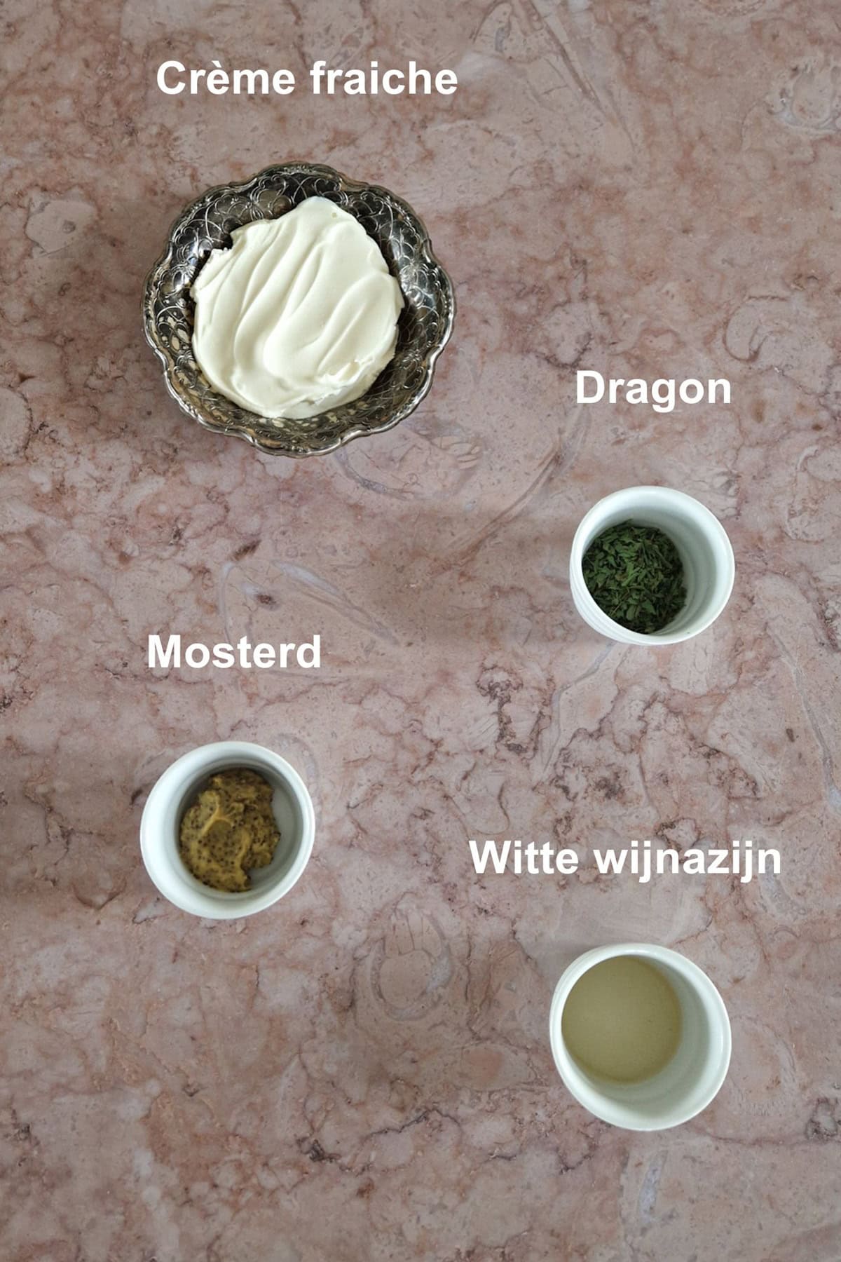 De ingrediënten voor snelle bearnaise: creme fraiche, dragon, mosterd, witte wijnazijn. De ingrediënten zijn uitgestald op een marmeren ondergrond.
