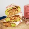 Tonijnwrap met avocado, een torentje van drie gestapelde, goed gevulde tonijnwraps met avocado. De wraps zijn dichtgebonden met een rood-wit keukentouwtje.