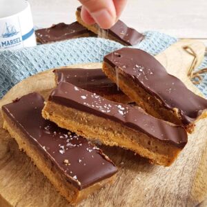 Een hand bestrooid chocolade karamel repen (Twix repen) met grof zeezout.