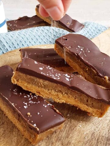 Een hand bestrooid chocolade karamel repen (Twix repen) met grof zeezout.