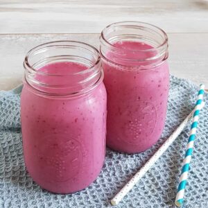 Milkshake zonder ijs met kersensmaak, voor het glas met de milkshake liggen twee rietjes op een blauwe doek.