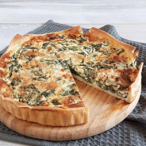 Quiche met spinazie en blauwe kaas op een houten serveerplank. Uit de quiche is een punt gesneden zodat je de vulling goed kunt zien.