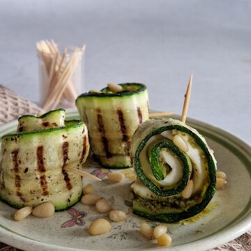 Drie courgette hapjes op een bordje. Twee rolletjes staan rechtop en één ligt op zijn kant, zodat je de inhoud van het courgetterolletje goed kunt zien.