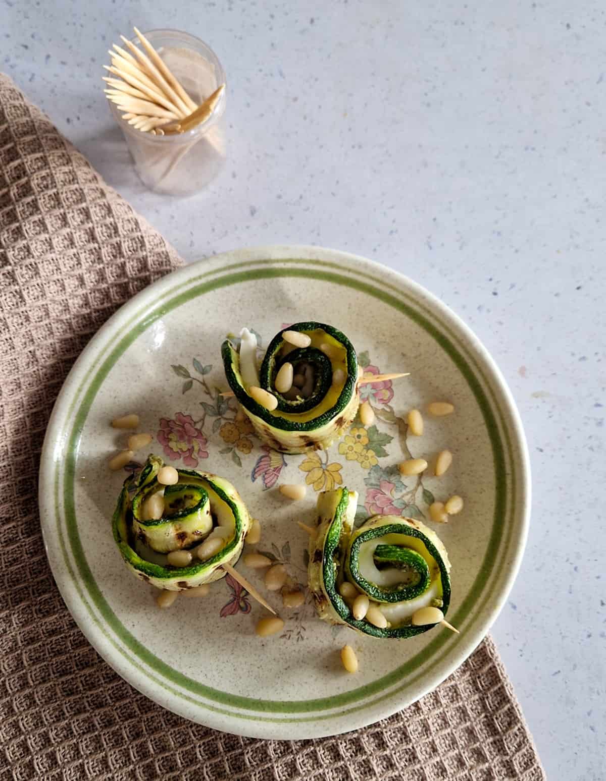 Bovenaanzicht van courgette met mozzarella en pesto. De courgette hapjes liggen op een klein bordje, met cocktailprikkers ernaast.