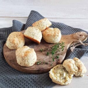 Hartige scones met tijm op een houten serveerplank. Eén scone is opengesneden en besmeerd met kruidenboter.