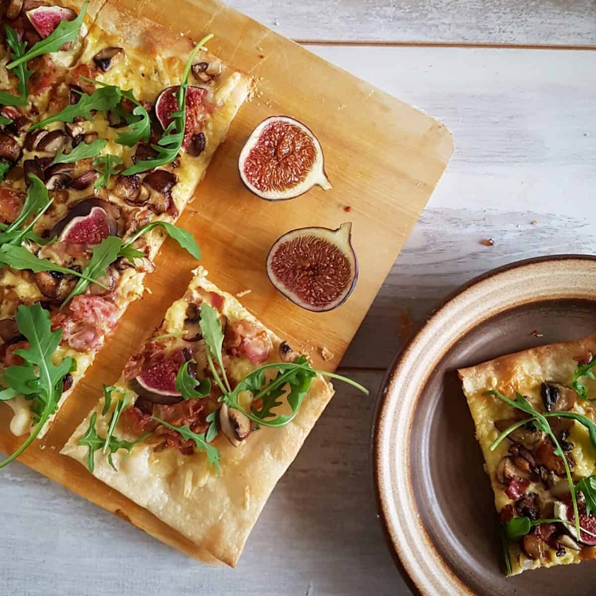 Flammkuchen met bacon en champignons, in stukken gesneden met een bordje met een punt flammkuchen ernaast.
