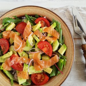 Salade met gerookte zalm, avocado en tomaat op een bruin bord.