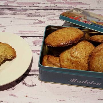 Een geopende koektrommel met gevulde koeken, met ernaast een gevulde koek op een bordje. Uit de koek is een hap genomen.