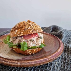 Broodje tonijnsalade met ingelegde radijs en wat verse sla, op een ouderwets bordje.