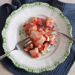 Kip met bacon - rolletjes op een bord, een vork waar een rolletje opgeprikt zit, wordt omhoog gehouden naar de camera.