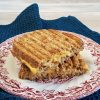 Tuna Melt Tosti op een ouderwets bordje. De tonijntosti met kaas is gehalveerd zodat je de vulling van tonijnsalade en cheddar goed kunt zien.