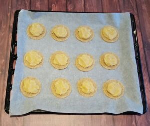 Een bakplaat met rondjes ongebakken koekdeeg met daarop een spijsvulling, als basis voor de gevulde koeken.