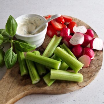 Een borrelplank met bleekselderij met dipsaus en andere groenten.