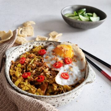 Een kom nasi goreng met een spiegelei en kroepoek.