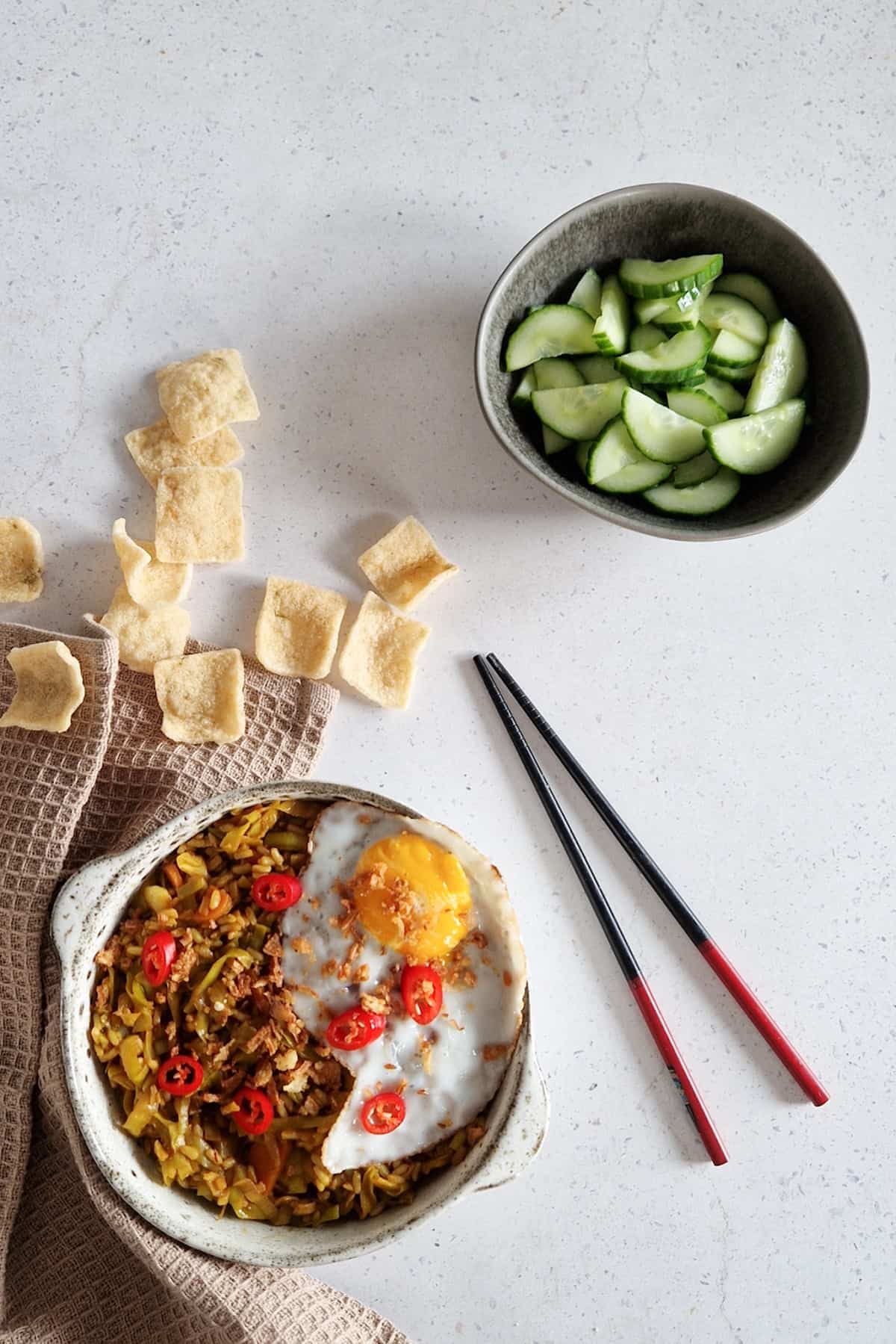 Een kom nasi goreng met bijgerechten (zoetzure komkommer, kroepoek en een spiegelei)
