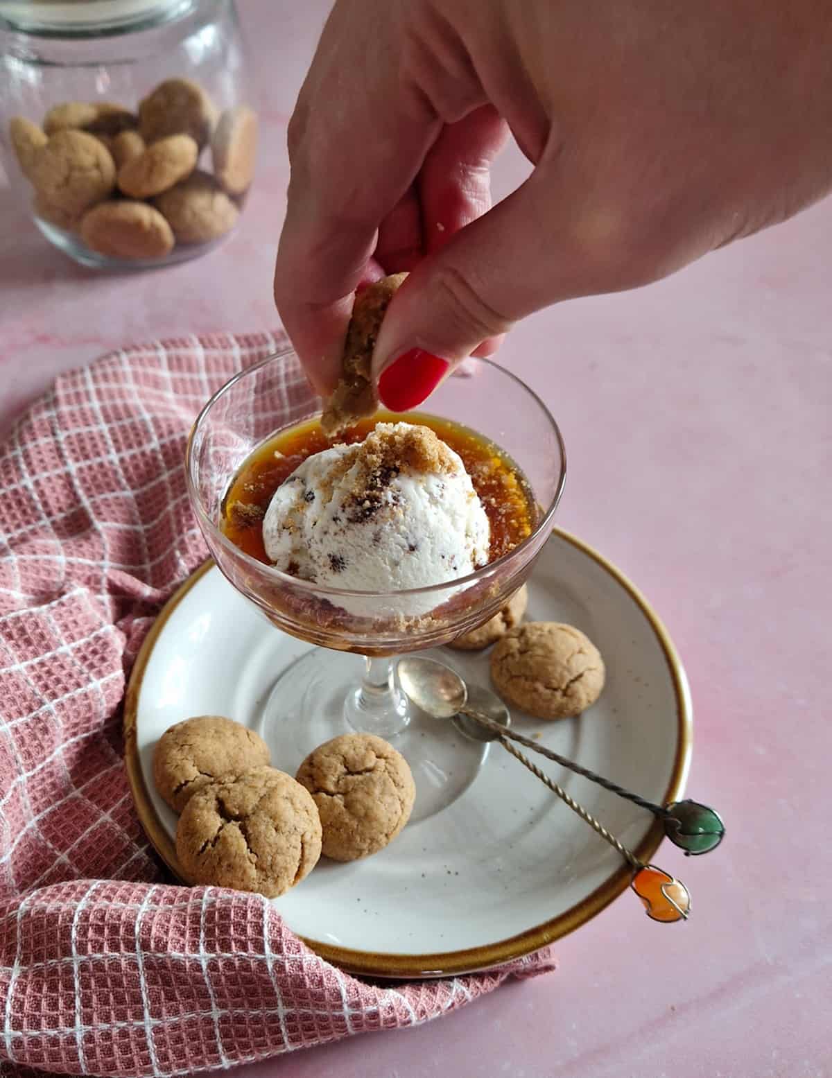 Een hand verkruimelt koekjes boven een glas met affogato, een Italiaans toetje van espresso met vanille-ijs.