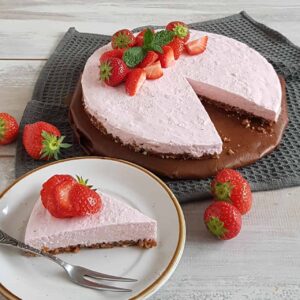 Ontbijttaart met aardbeien. Van de ontbijttaart is een punt afgesneden dat op een gebaksbordje ligt, waardoor je ook de bodem die onder andere van dadels is gemaakt, goed kunt zien. De taart is gegarneerd met verse aardbeien.