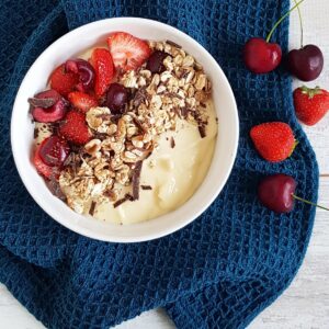 Smoothiebowl met mango en banaan. De gele smoothiebowl is gegarneerd met granola, aardbeien, kersen en stukjes chocolade.