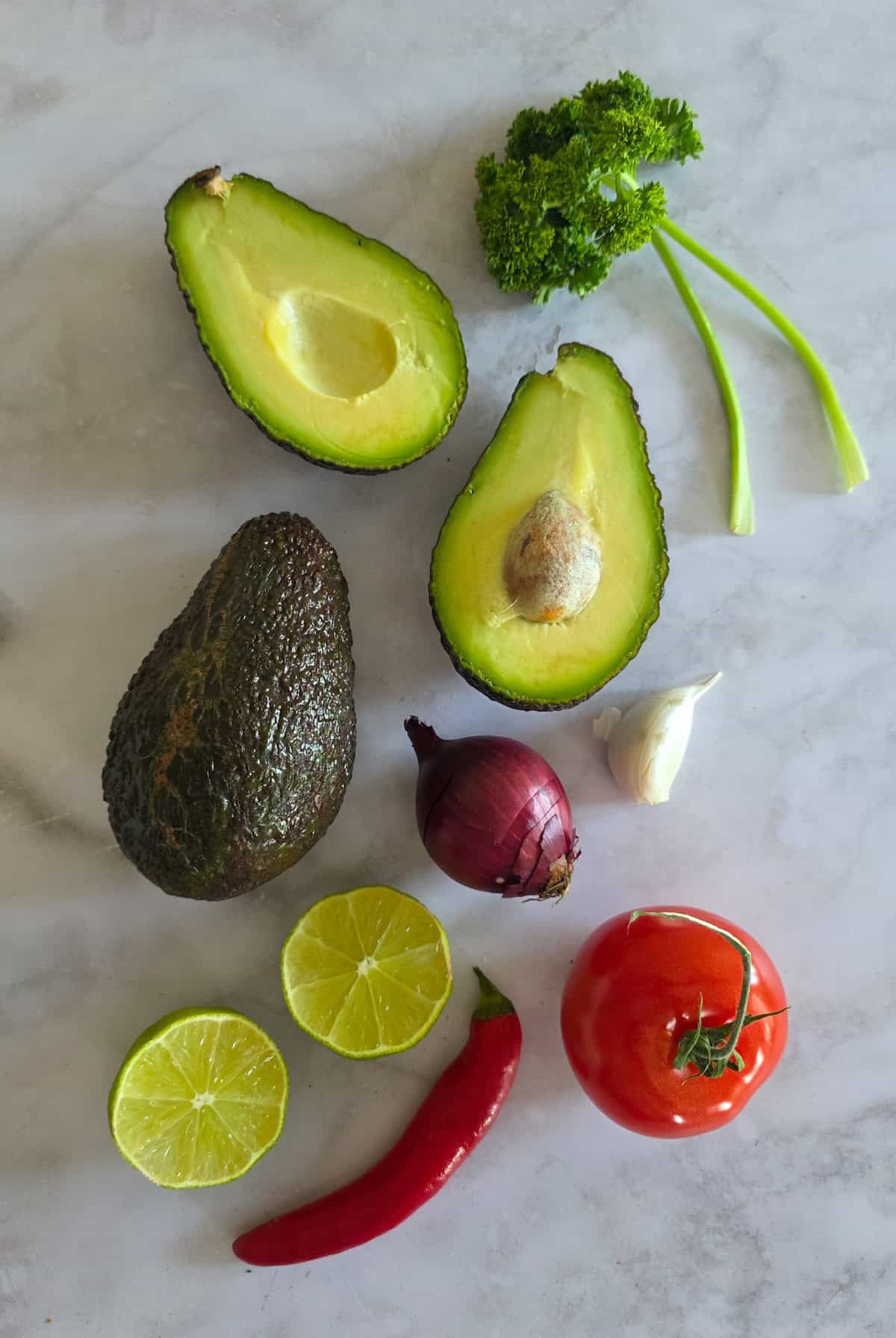 De ingrediënten om guacemole te maken, uit gestald op een witmarmeren ondergrond.