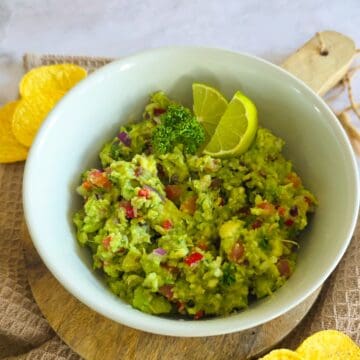 Een kom met zelfgemaakte guacemole met rode peper, tomaat, ui en knoflook.