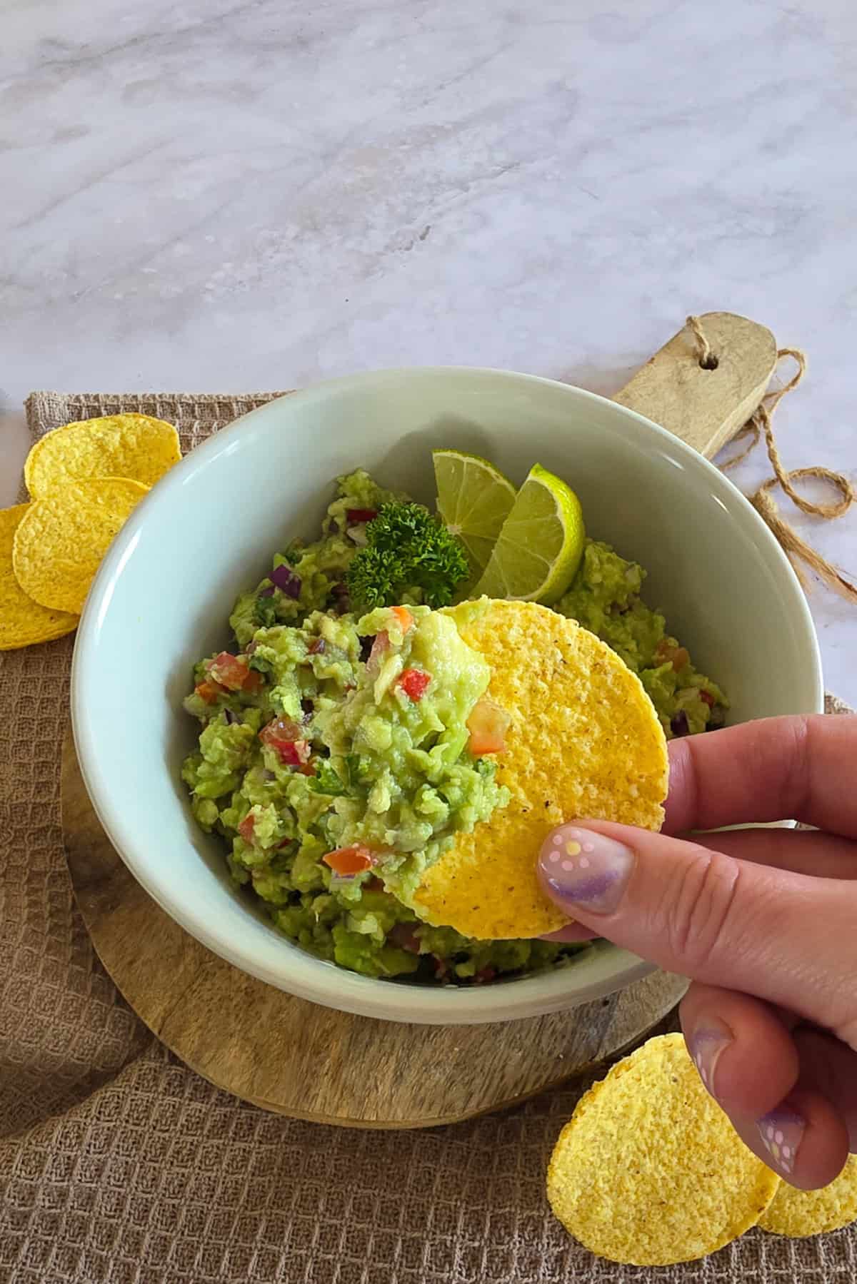Een hand houdt een nachochipje met zelfgemaakte guacemole omhoog.