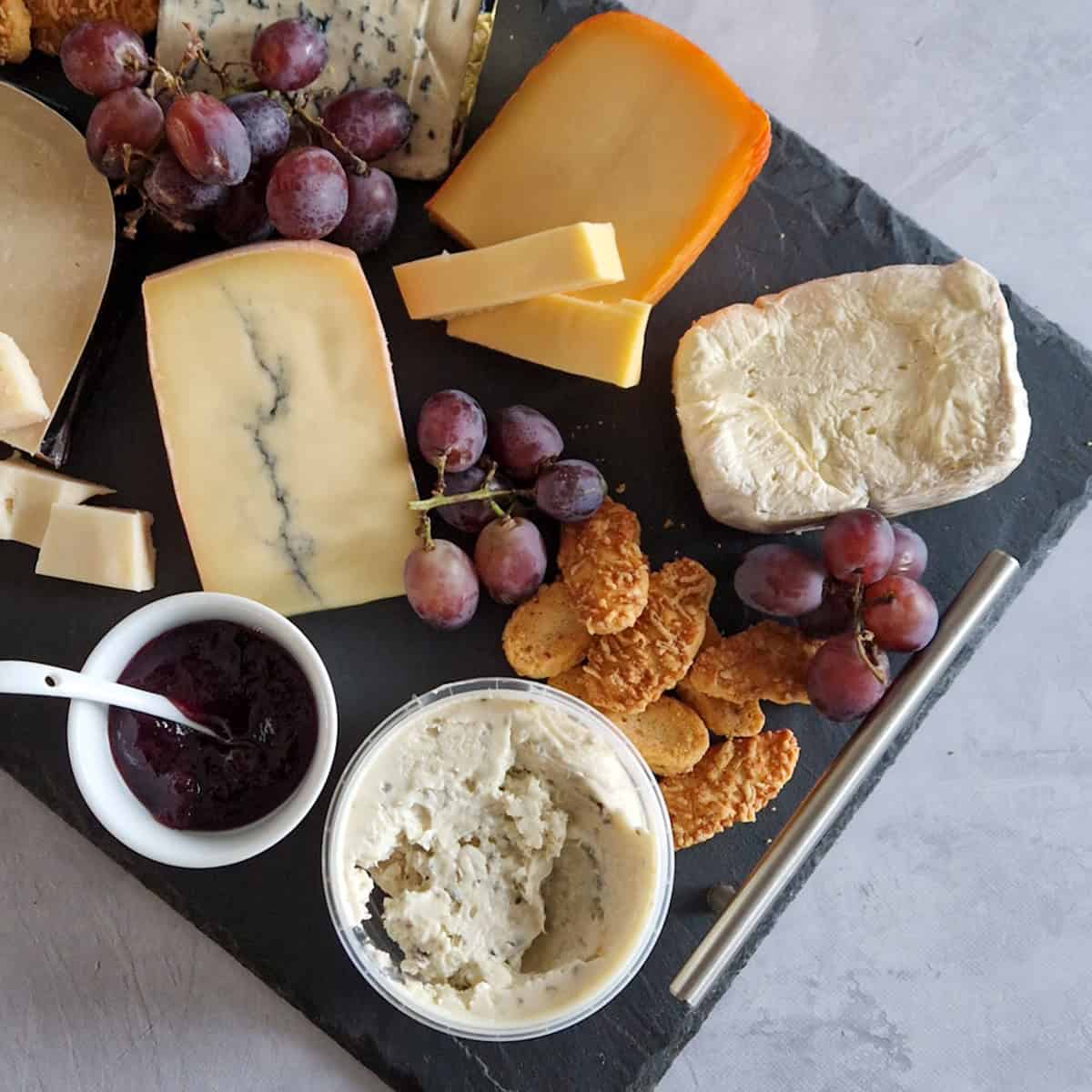 Kaasplankje maken met verschillende kazen en bijgerechten. Op deze kaasplanken liggen zes kazen, crackers en druiven.