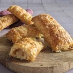 Zelf kaasbroodjes maken met als resultaat deze kaasbroodjes op een houten serveerplank. Het voorste broodje is opengesneden zodat de kaasvulling zichtbaar wordt.