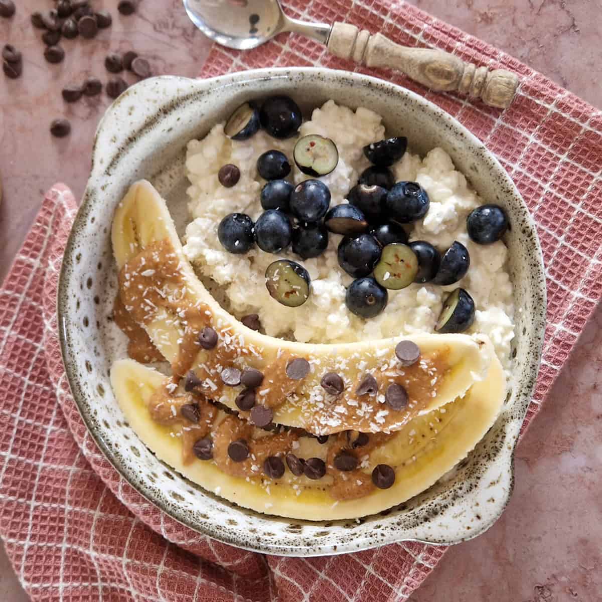 Een banaan cottage cheese snack in een gespikkelde schaal, op een oudroze doek.