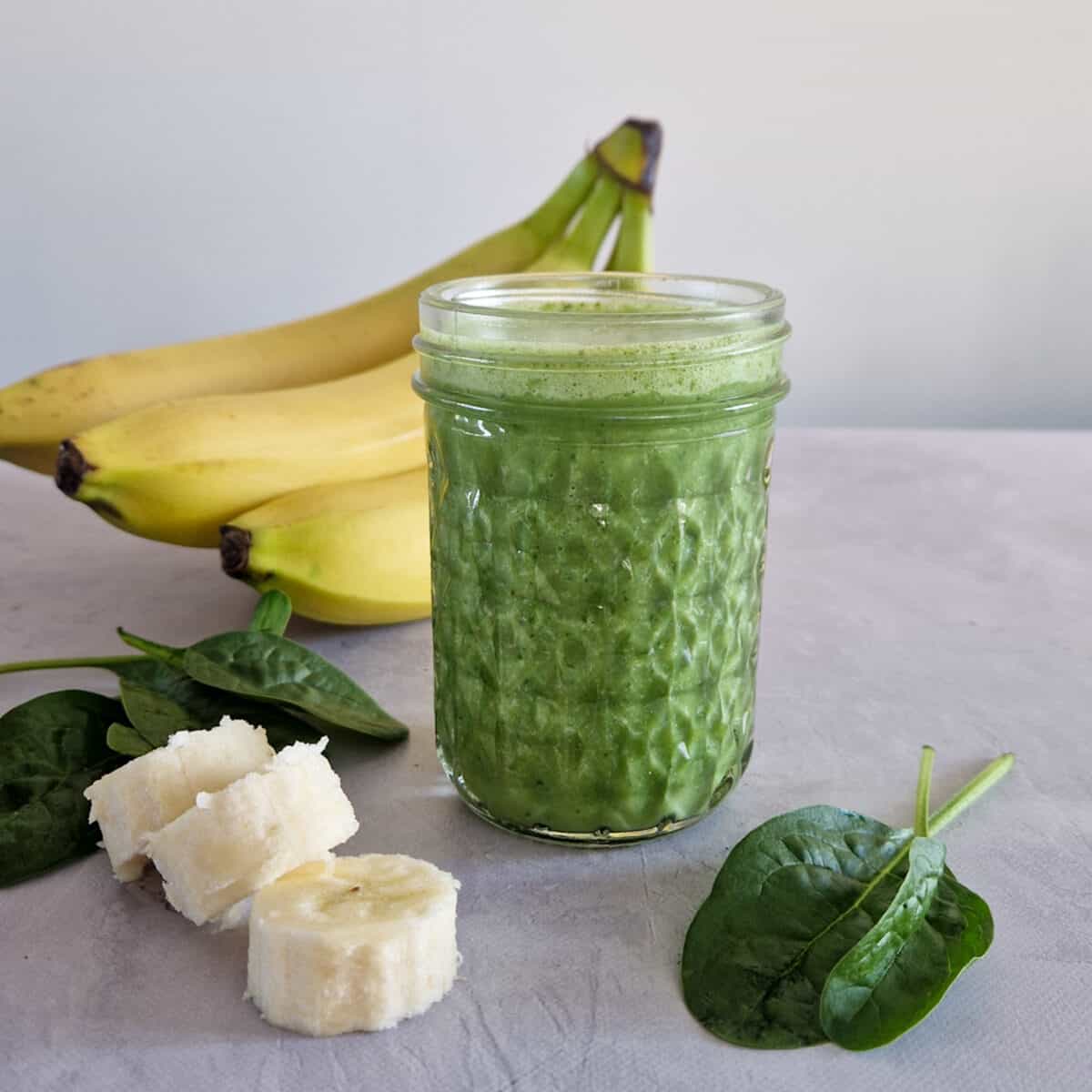 Smoothie met spinazie en banaan in een doorzichtig glas. Om het glas heen liggen banaan en spinazie.