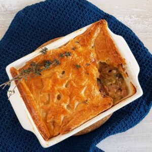 Pastei met ham en prei. De pastei is aan de bovenkant opengemaakt zodat je de vulling kunt zien. Het bladerdeeg is versierd met sterren van bladerdeeg.