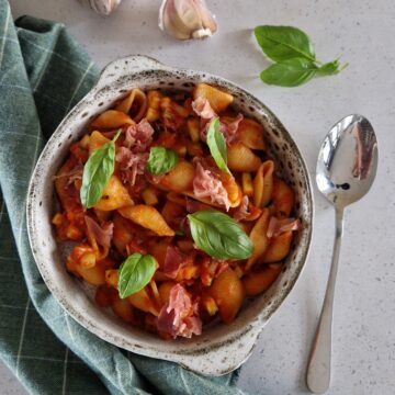 Tomaten courgette saus met pasta, rauwe ham en basilicum in een kom.