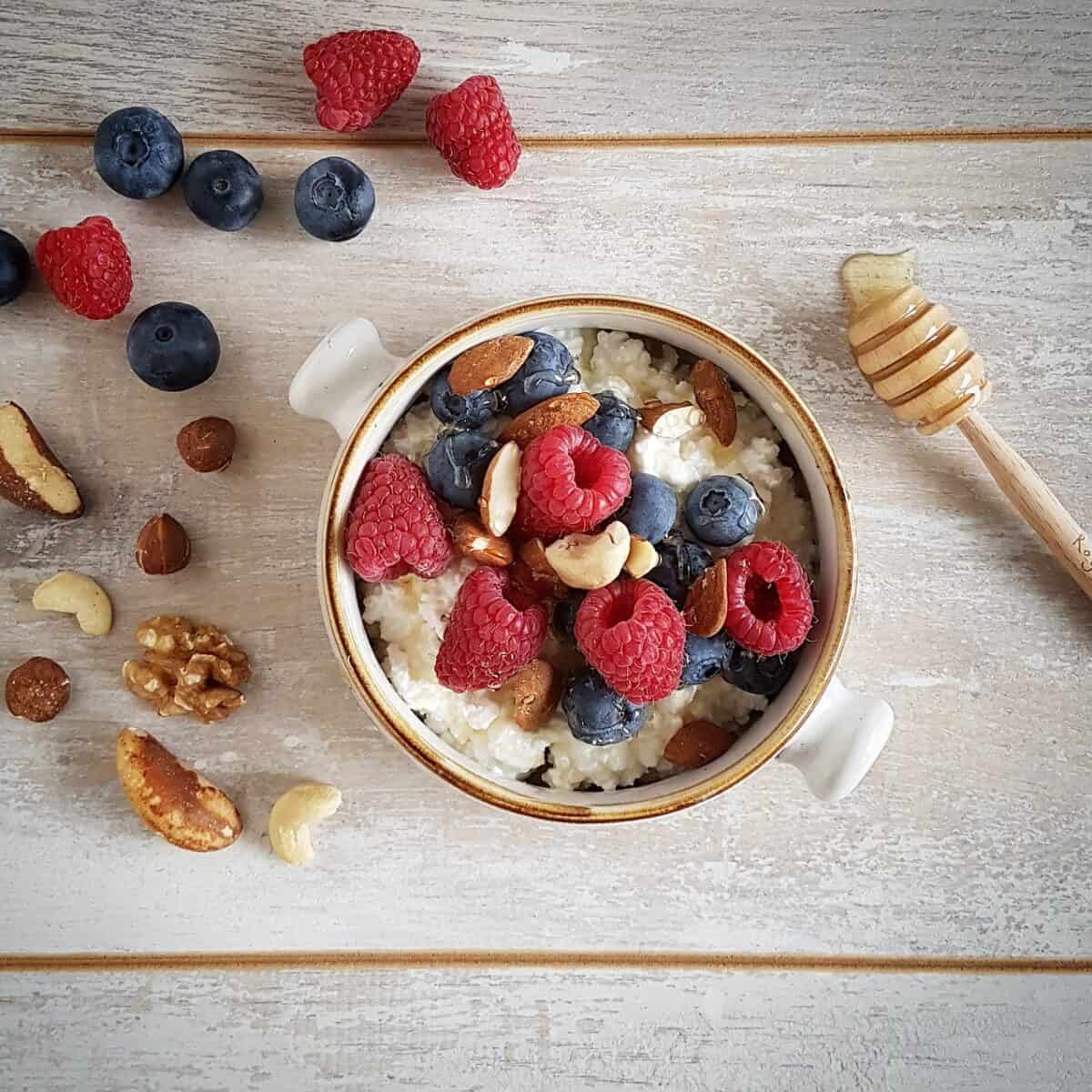 Een cottage cheese ontbijt met fruit en noten in een kom. De cottage cheese is gegarneerd met veel vers fruit en er liggen noten naast ter decoratie.