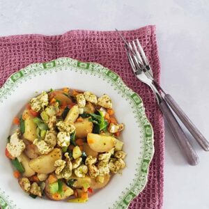 Kipschotel met aardappel en wokgroenten op een bord met decoratieve groene rand.