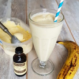 Milkshake banaan & vanille in een milkshakeglas. De ingrediënten van het recept staan er omheen: ijs, vanillepasta en banaan.