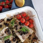 Zeewolf recept uit de oven: een ovenschaal met een stuk vis dat is bedekt met olijven, kappertjes en venkelloof. De witvis ligt op reepjes venkel.