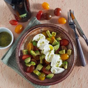 Tomatensalade met avocado en mozzarella. De salade is besprenkeld met een pestodressing.