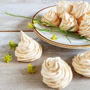 Een bordje met vanille meringue met eetbare bloemen, gedecoreerd met koolzaad bloemen.