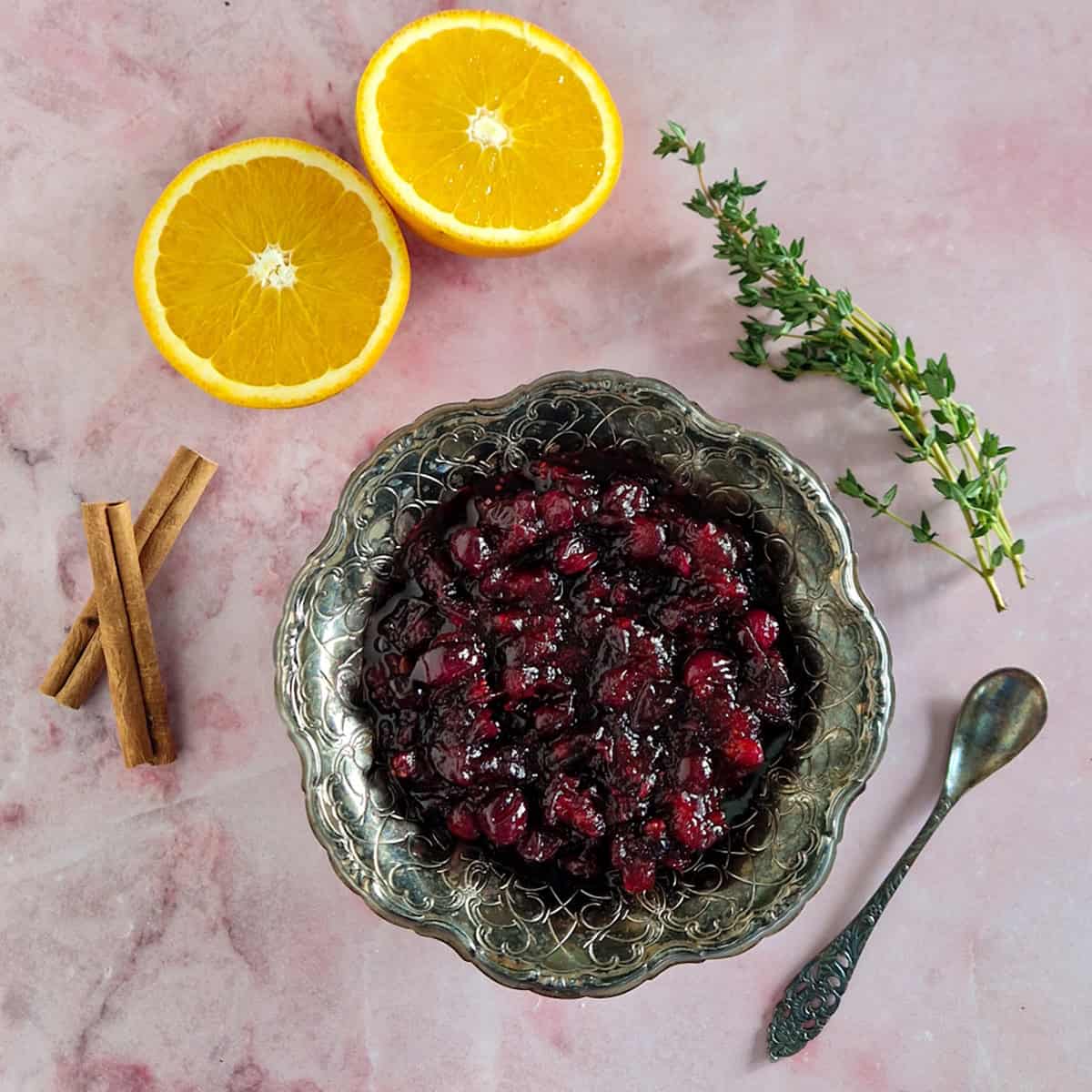 Cranberrycompote met kaneel en tijm in een kommetje. Er ligt een kaneelstokje en verse tijm op als garnering.