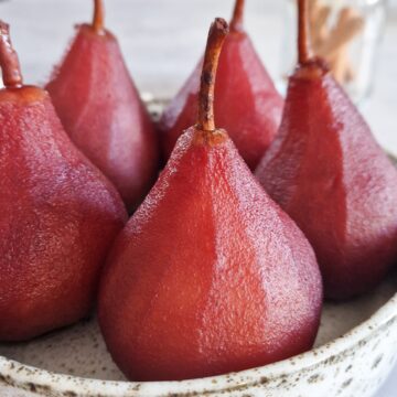Stoofperen met port, kaneel en kardemom op een bord. Op de achtergrond een potje kaneelstokjes.