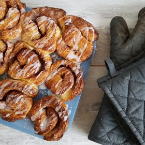 Kaneelbroodjes - Cinnamon rolls met een frosting van poedersuiker en water. De broodjes zitten nog in de muffinvorm waarin ze gebakken zijn.
