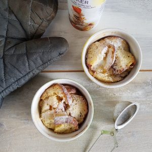 Broodpudding van oliebollen in twee kleine ovenschaaltjes. De oliebollen broodpuddinkjes zijn bestrooid met poedersuiker.