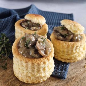 Champignon ragout pasteitjes op een houten plank. Op één van de pasteitjes zit een dakje van bladerdeeg. De pasteitjes zijn bestrooid met verse tijm.