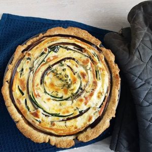 Spiraaltaart met courgette, aubergine, wortel en brie. De groenten zijn in een spiraalvorm in de quichevorm gelegd met plakken brie ertussen, waardoor een spiraaleffect ontstaat.