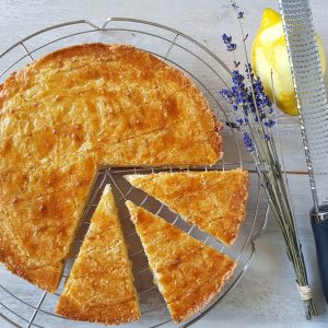 Boterkoek met citroen en lavendel, uit de boterkoek zijn drie punten gesneden. Naast de stukken koek liggen een gehalveerde citroen en een bosje lavendel.