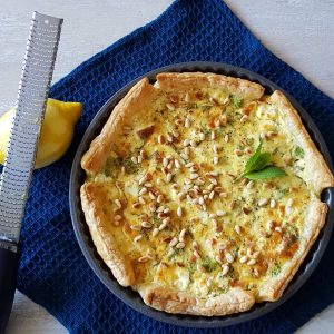 Brandnetelquiche met brandnetel, kaas en pijnboompitten. De quiche zit nog in de bakvorm.